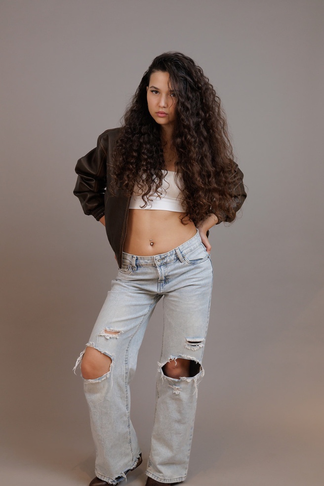נערה עם שיער מתולתל בג'ינס קרוע וז'קט, גוף מלא בסטודיו